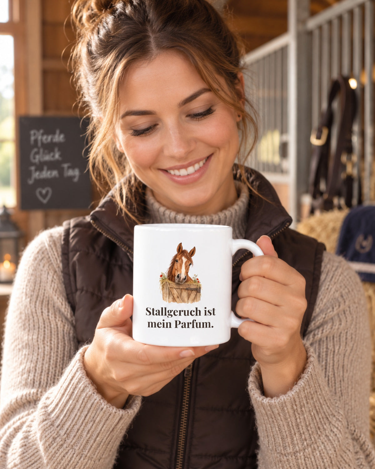 Reiterin im Stall hält die Tasse „Stallgeruch ist mein Parfum.“ mit Pferdekopf über der Boxentür