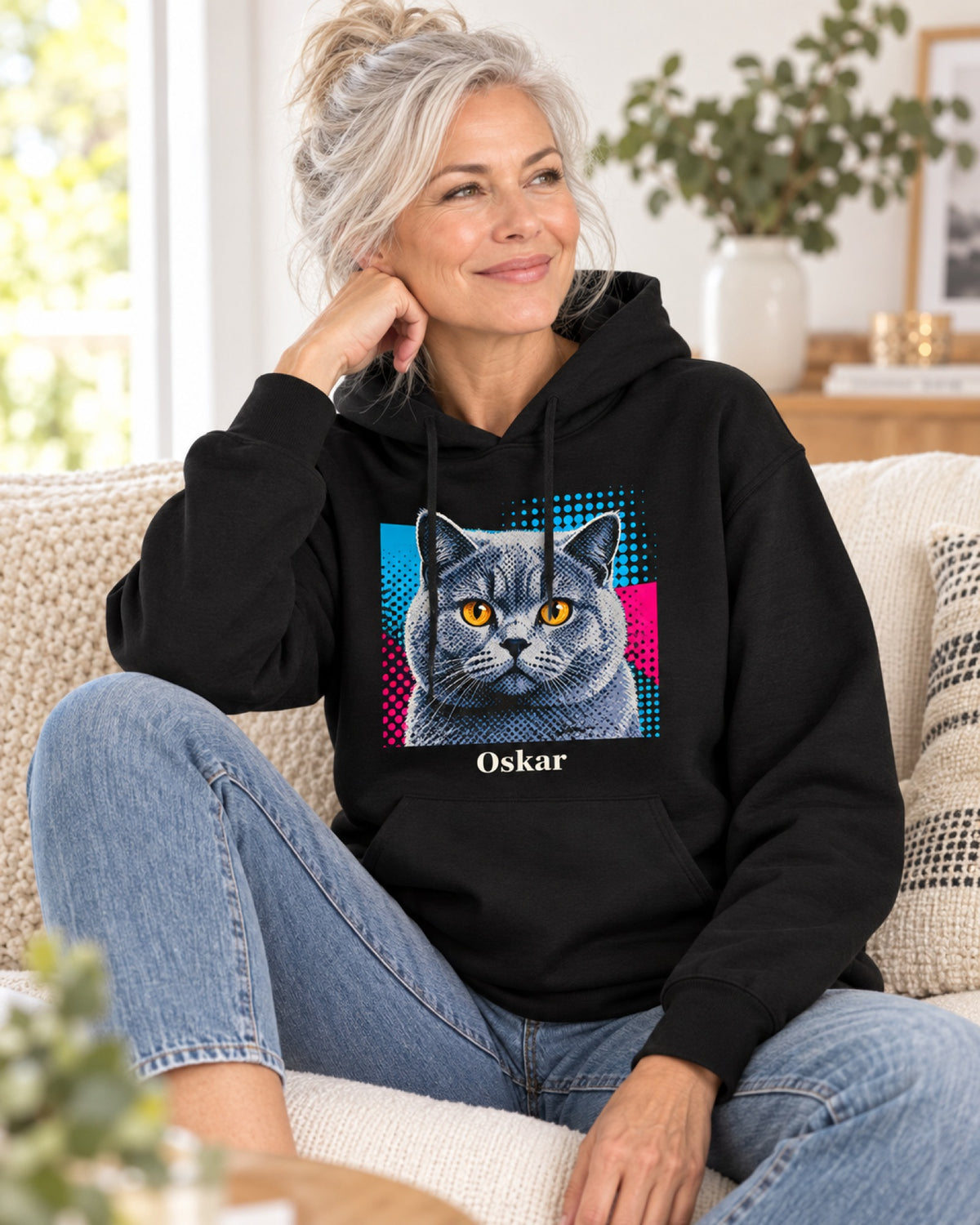 Schwarzer Hoodie mit Britisch Kurzhaar im Pop-Art-Stil und Namen Oskar, eine Frau sitzt entspannt auf dem Sofa