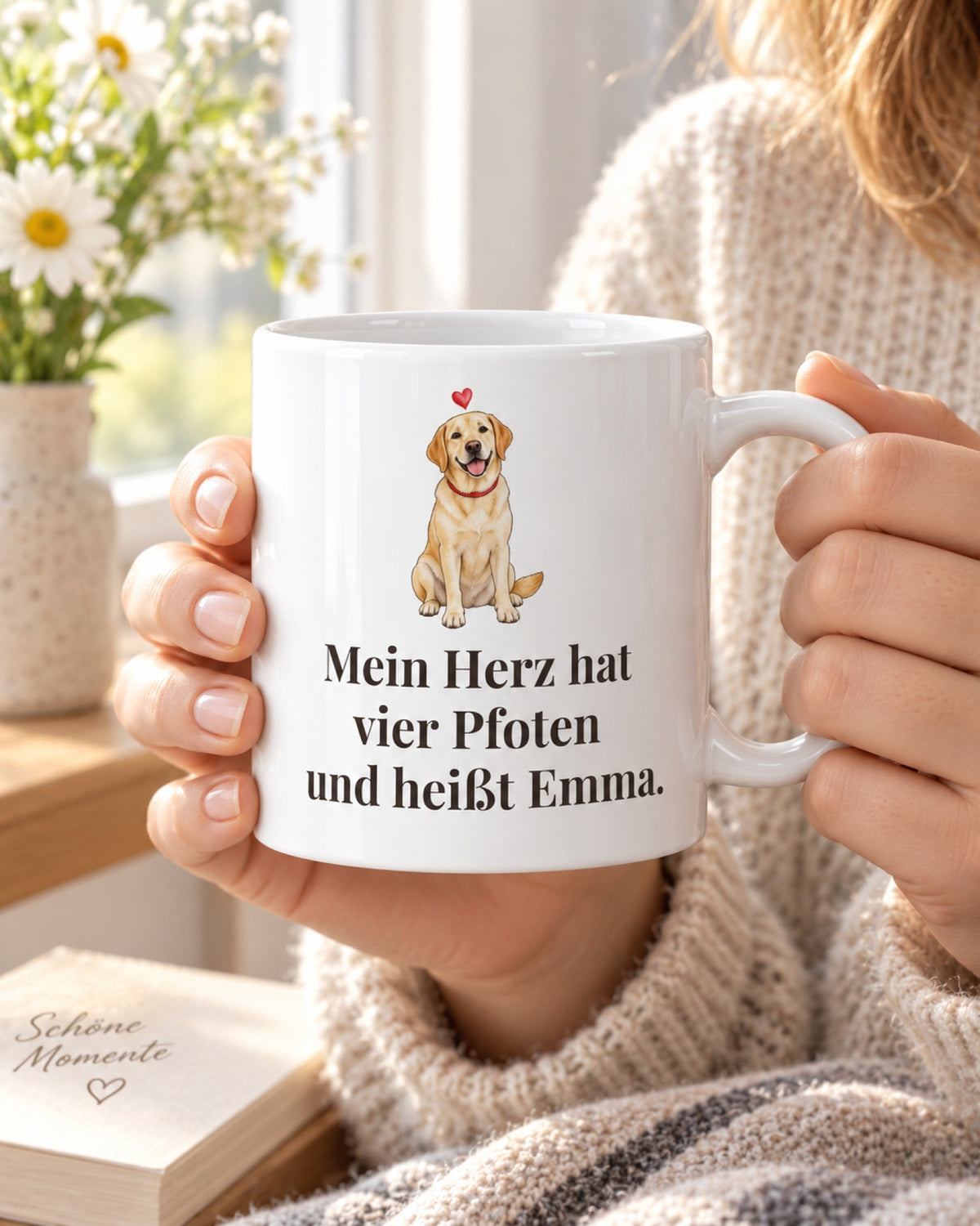 Hände halten die Tasse „Mein Herz hat vier Pfoten und heißt Emma.“ mit Labrador am hellen Fenster
