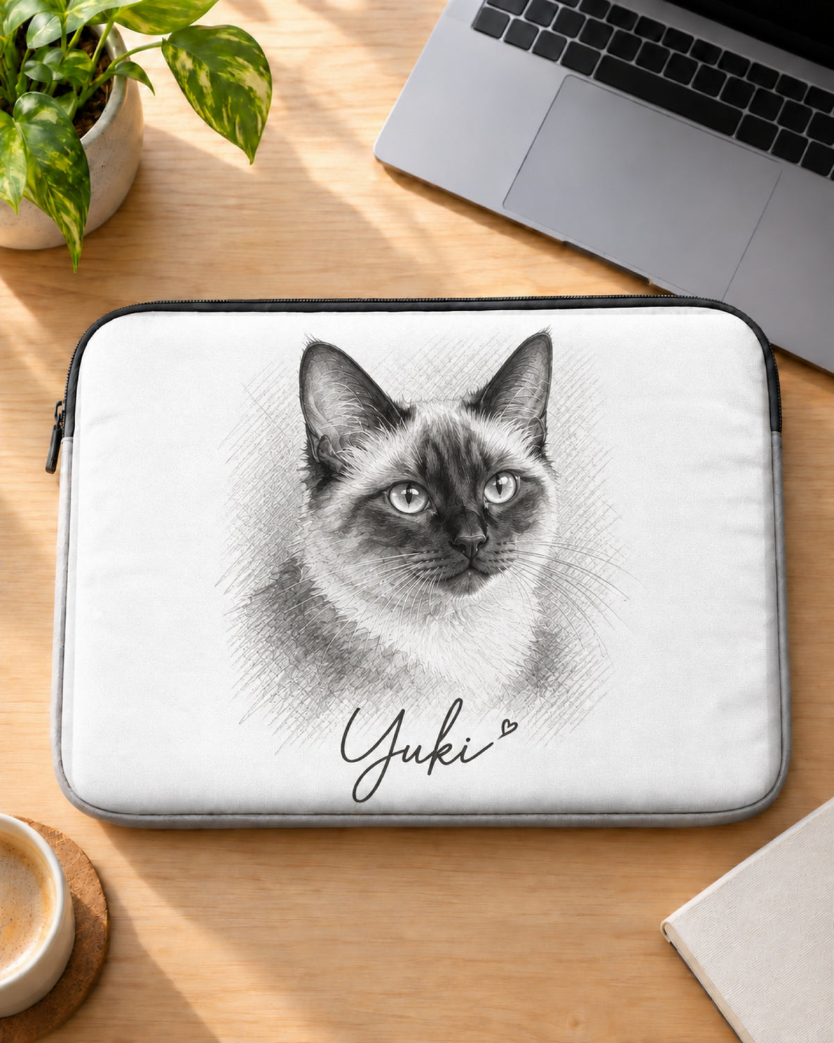 Weiße Laptophülle mit Siamkatze im Sketch-Stil und dem Namen Yuki auf dem Schreibtisch neben dem Laptop