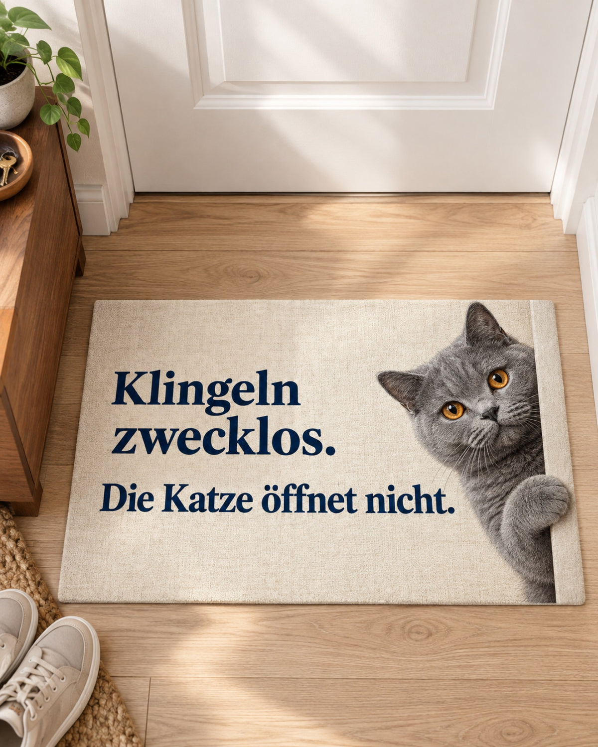 Fußmatte mit dem Spruch Klingeln zwecklos. Die Katze öffnet nicht. und grauer Kartäuserkatze im hellen Flur innen