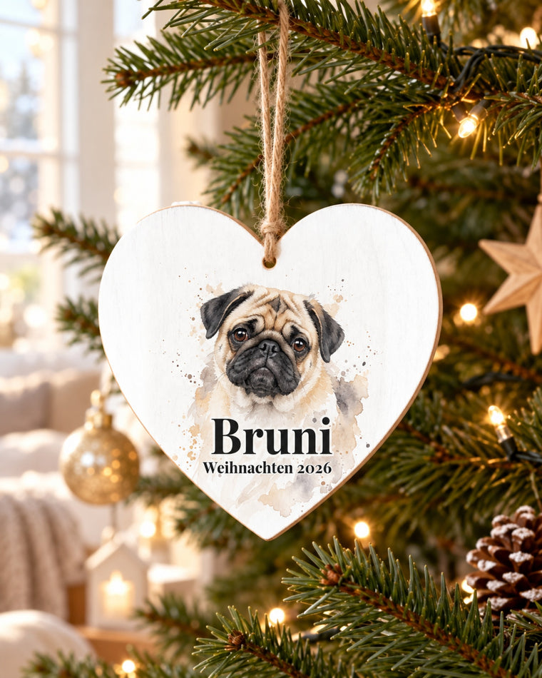 Herzförmiger Baumschmuck aus Holz mit Mops im Aquarell-Stil und Namen Bruni, am Tannenbaum im weihnachtlichen Wohnzimmer