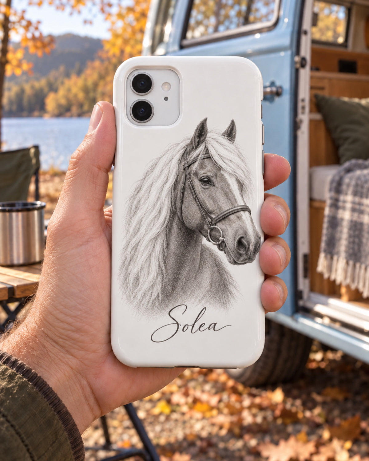 iPhone 11 Hülle mit Haflinger Solea im Sketch Stil in einer Hand am hellblauen Campingbus im Herbst