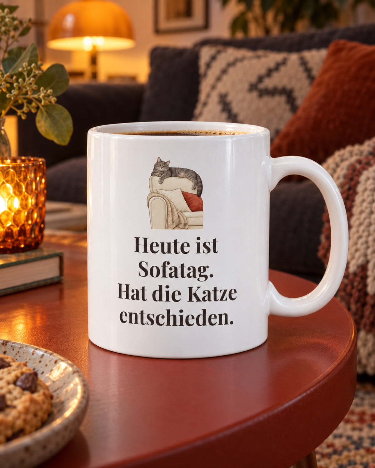 Weiße Keramiktasse Katzentasse mit Spruch: Heute ist Sofatag. Hat die Katze entschieden. auf einem roten Couchtisch am Abend