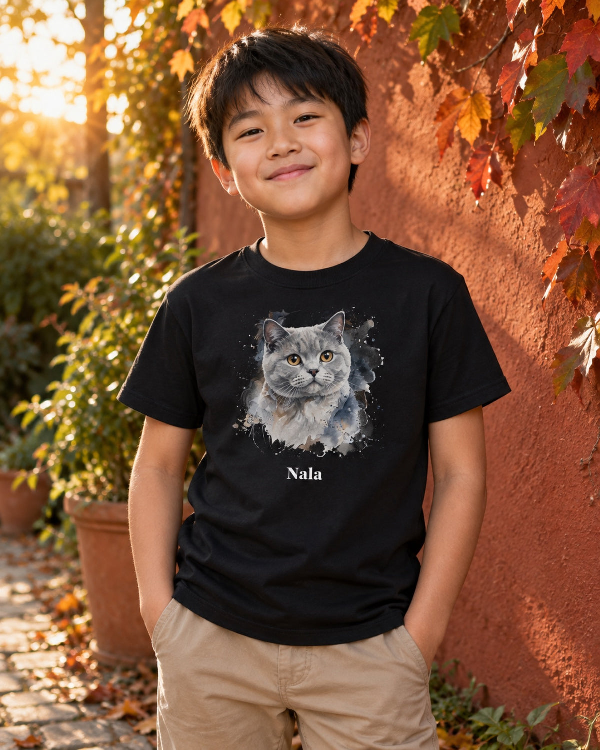 Junge im schwarzen Kinder-T-Shirt mit grauer Britisch Kurzhaar Nala als Aquarellportrait an einer herbstlichen Gartenmauer