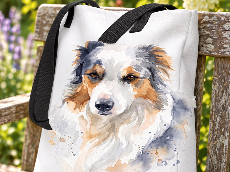 Weiße Stofftasche mit schwarzen Henkeln und Australian Shepherd im Aquarell-Stil auf einer Holzbank im Garten