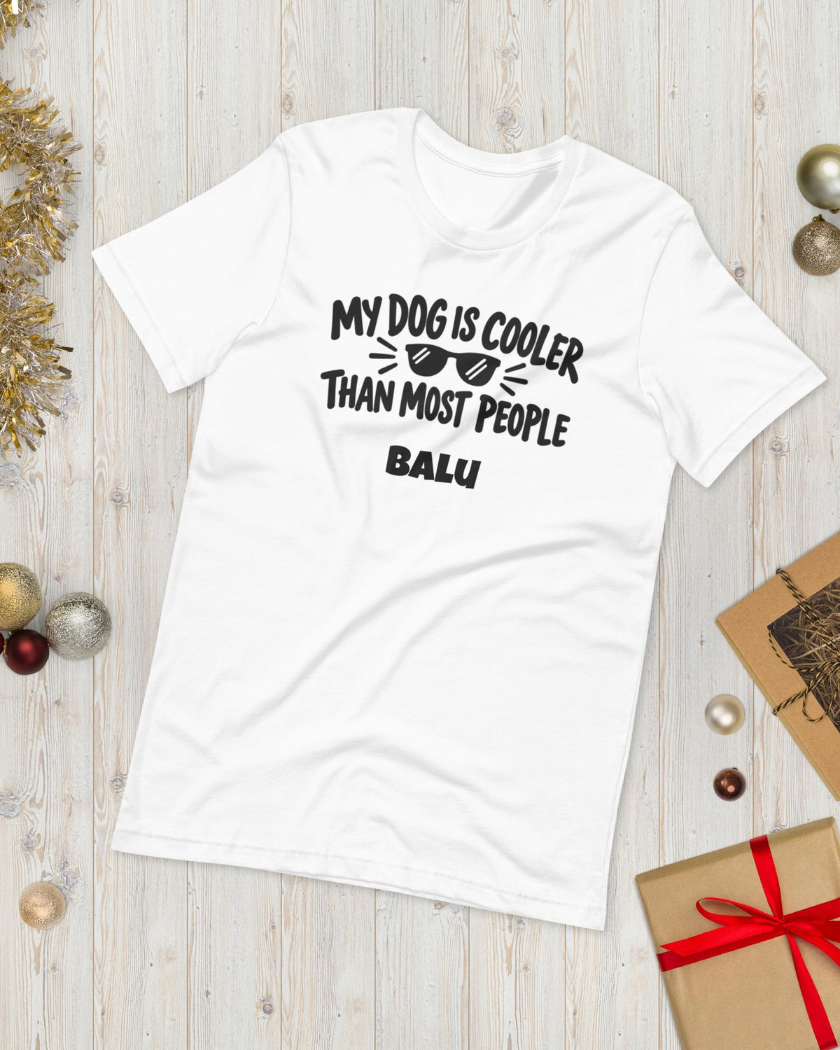 T-Shirt My Dog Is Cooler Than Most People in Weiß mit Namen Balu, weihnachtlich auf Holz gelegt