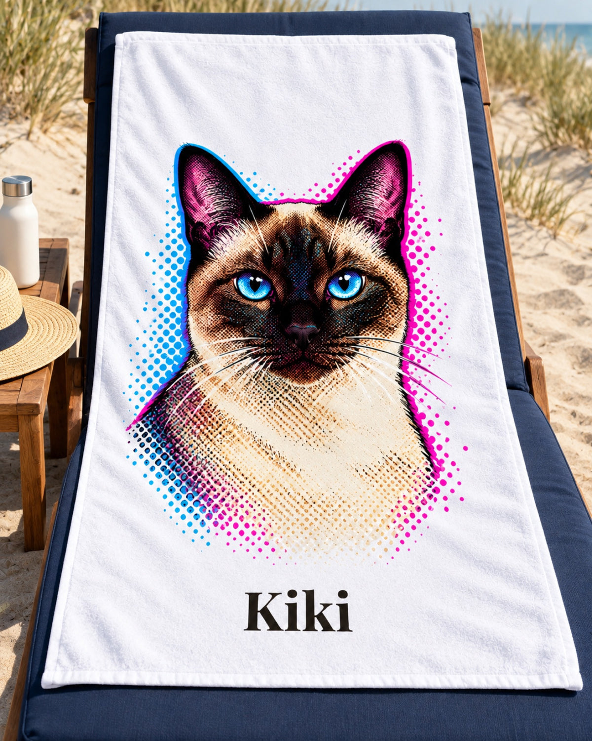 Badetuch mit Siamkatze im Pop-Art-Stil und Namen Kiki auf einer dunkelblauen Strandliege neben hellen Dünen